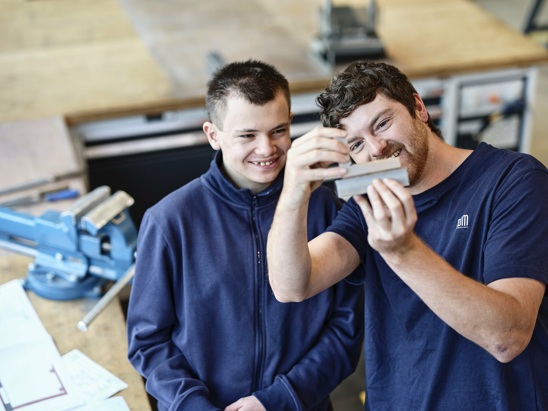 Lehrlingsausbildner aus dem Werkzeugbau prüft mit Lehrling ein gefertigtes Metallelement.