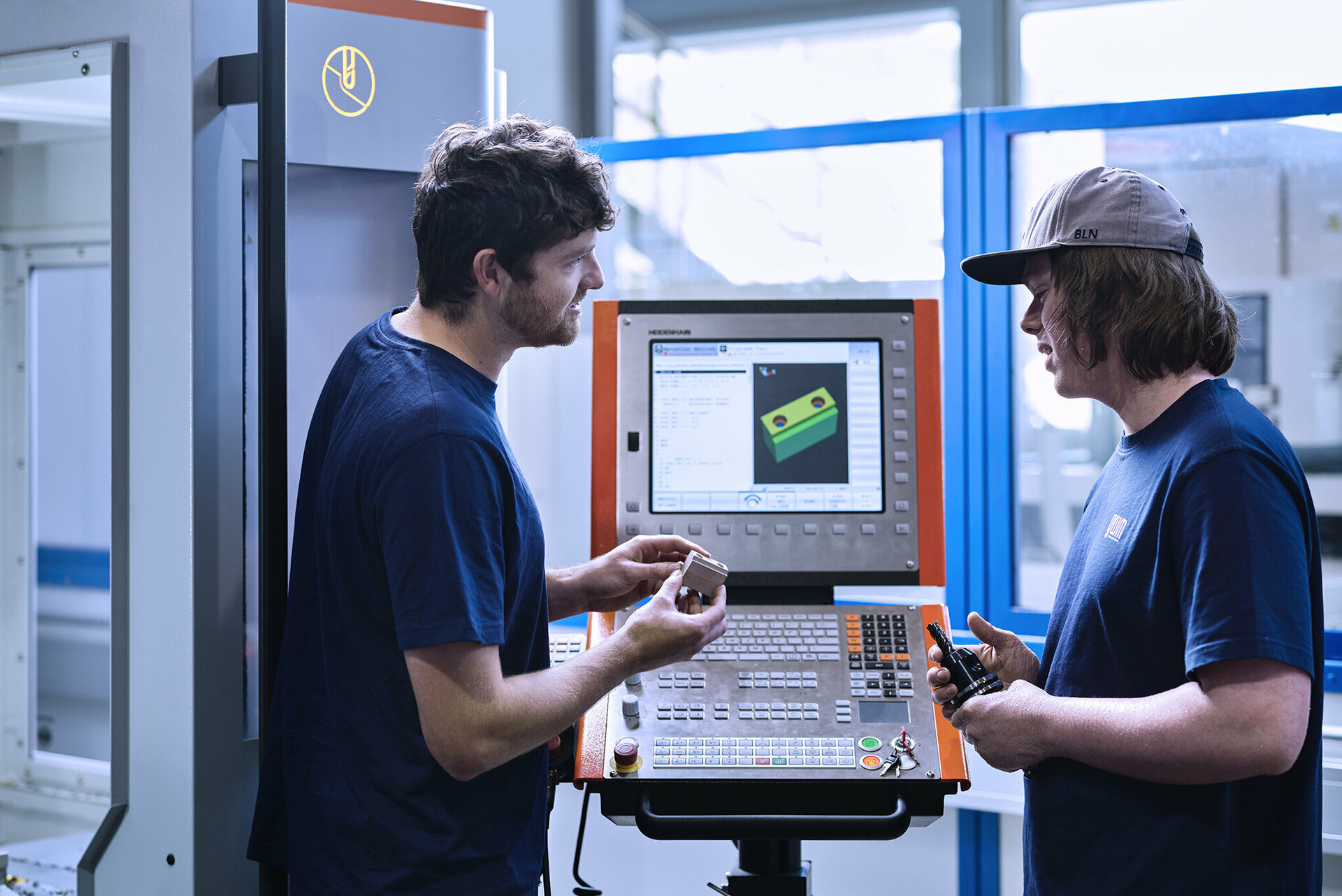 Lehrlingsausbildner aus dem Werkzeugbau und der Metalltechnik erklärt dem Lehrling die Fertigung eines Metallteils.