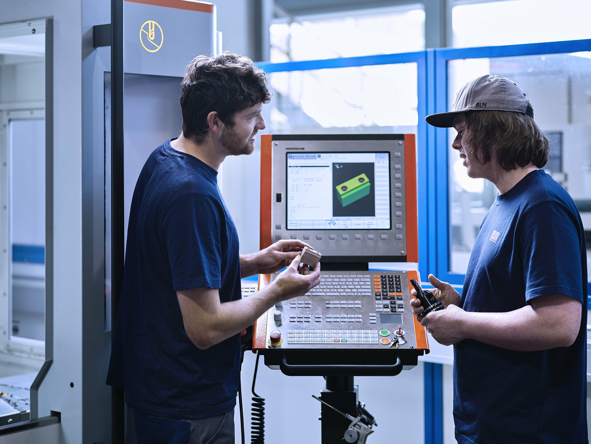 Lehrlingsausbildner aus dem Werkzeugbau und der Metalltechnik erklärt dem Lehrling die Fertigung eines Metallteils.