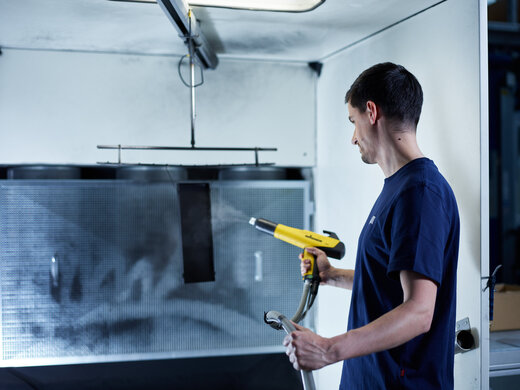 Mitarbeiter beschichtet Metallteil mit Pulverbeschichtungspistole